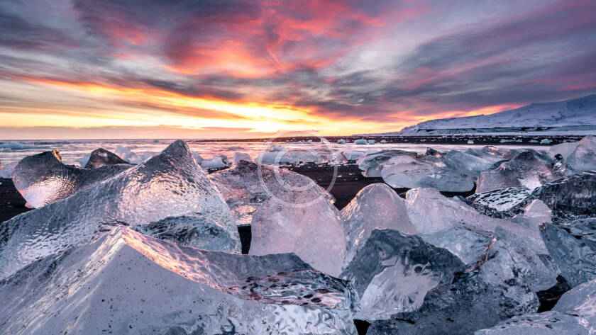 A sunset over the ocean with ice chunks in the foreground.