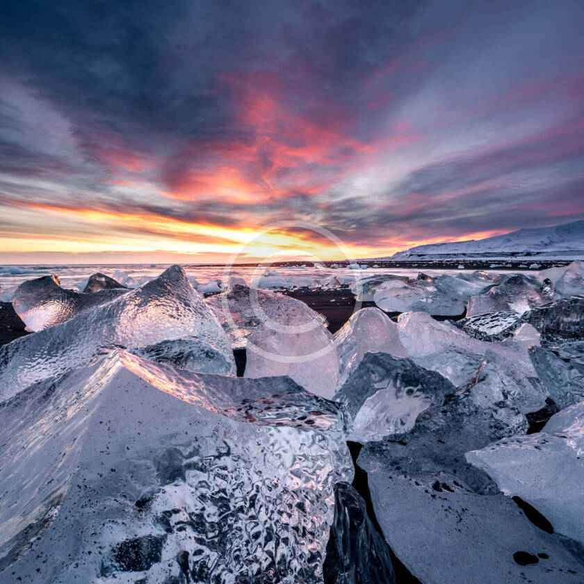 A sunset over the ocean with ice chunks in the foreground.