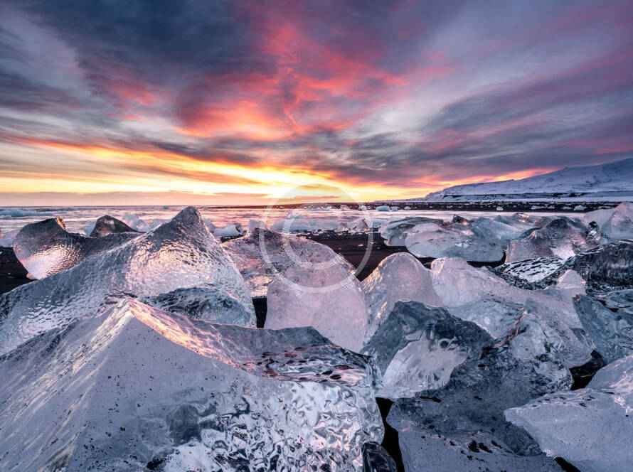 A sunset over the ocean with ice chunks in the foreground.