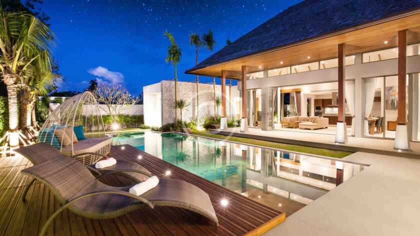 A pool with lounge chairs and a house in the background.