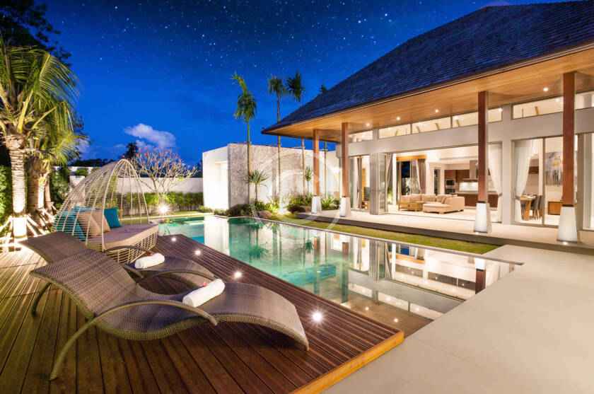 A pool with lounge chairs and a house in the background.