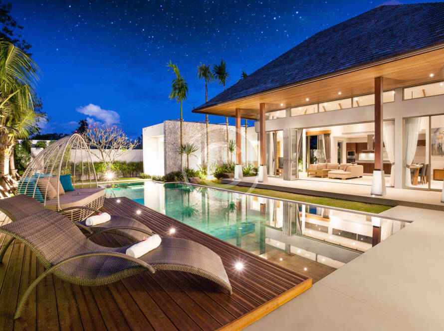 A pool with lounge chairs and a house in the background.