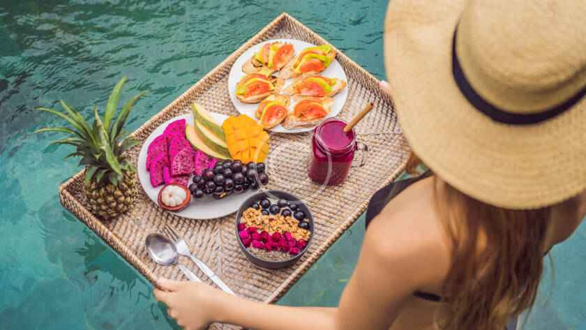 A woman in a hat and sunglasses holding a tray of food.