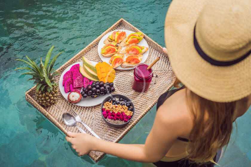 A woman in a hat and sunglasses holding a tray of food.