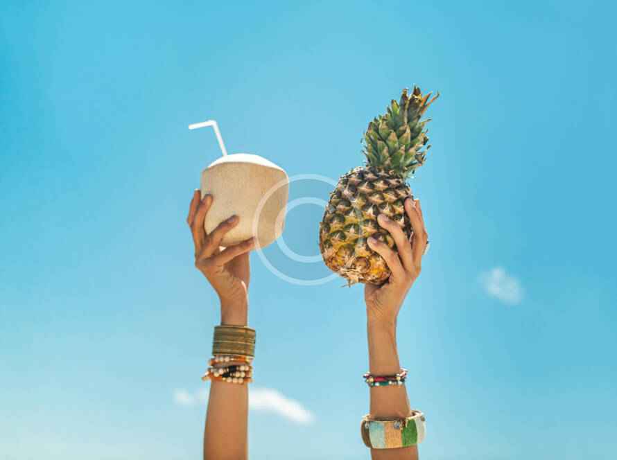 Two hands holding a pineapple and a drink.