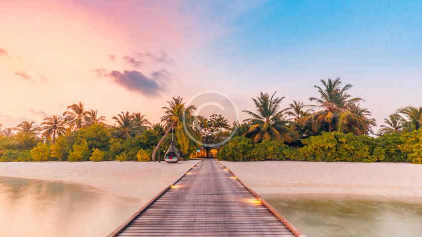 Tropical beach boardwalk under colorful sunset sky.