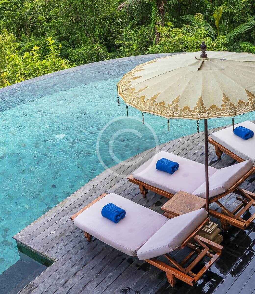 A pool with an umbrella and chairs by the water