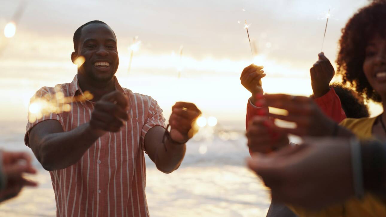 Beach, sparkler and group of people at party with happiness, celebration with friends on vacation.