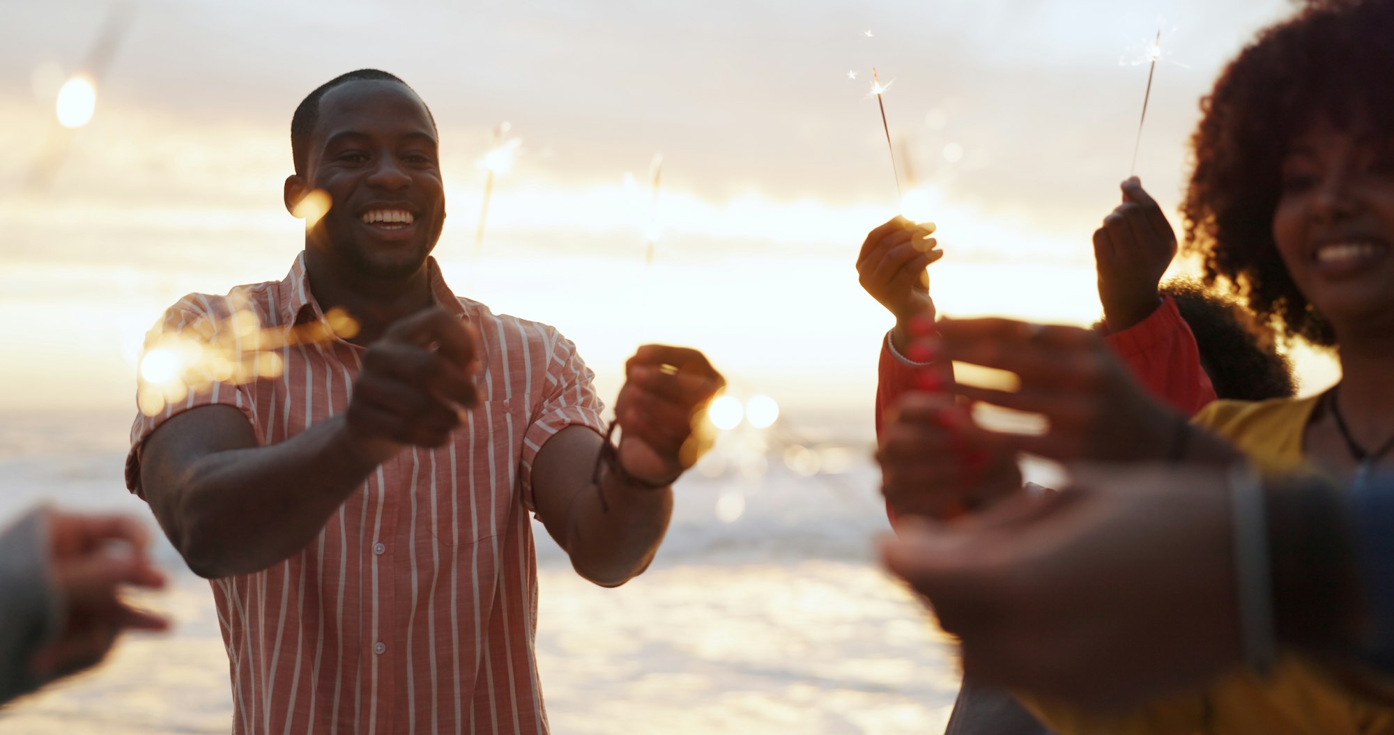Beach, sparkler and group of people at party with happiness, celebration with friends on vacation.