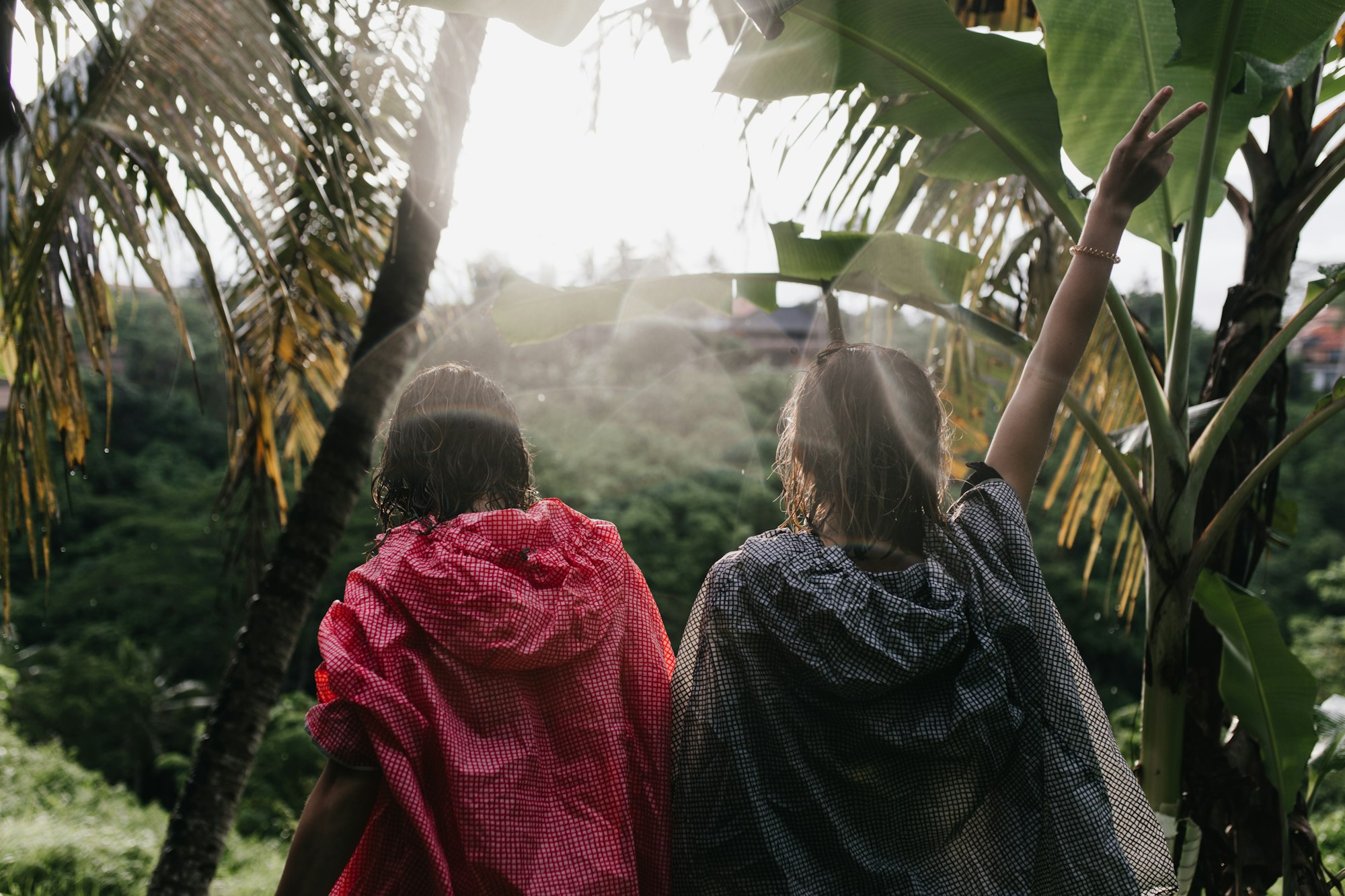 Brunette girl in pink raincoat exploring jungle with friend. Female tourists chilling during trip a