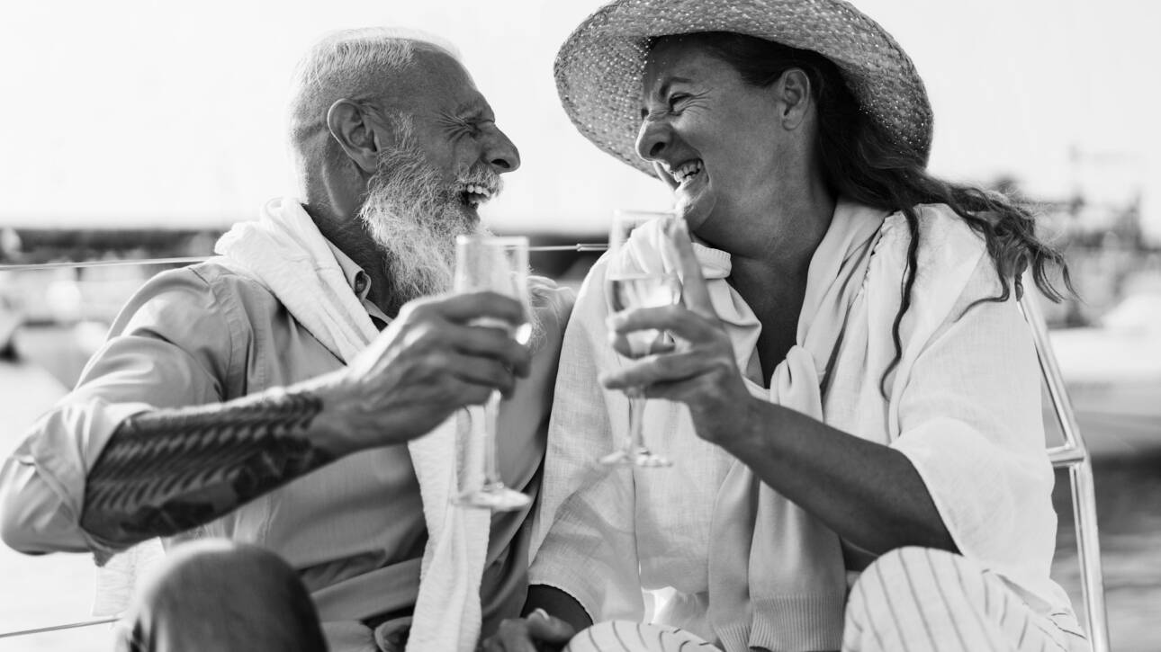 Senior couple cheering with champagne on boat during summer vacation