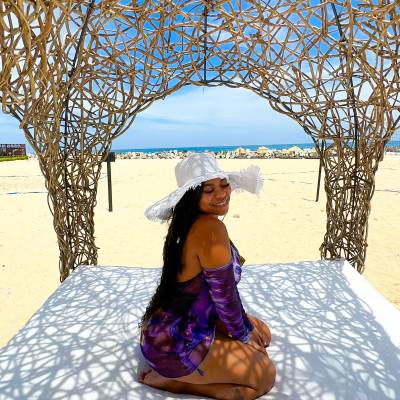 A woman sitting on top of a bed under an umbrella.
